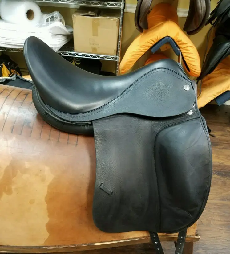 A black saddle sitting on top of a wooden floor.