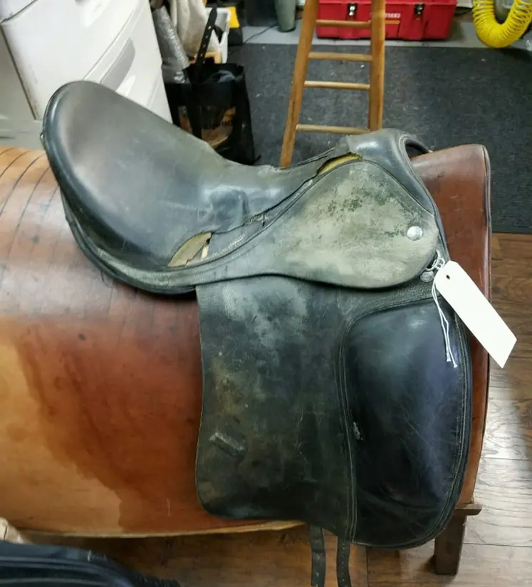 A saddle sitting on top of a brown leather bag.